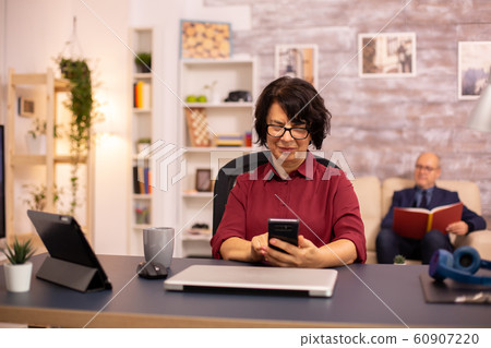 Old lady in her 60s using modern technolgy in cozy living space 60907220