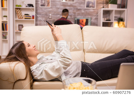 Beautiful young woman resting on sofa and browsing on sofa 60907276