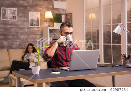 Handsome young man enjoying a cup of coffee while working on laptop 60907984