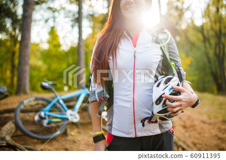 Photo of young sporty woman with helmet on background of bicycle at autumn forest 60911395