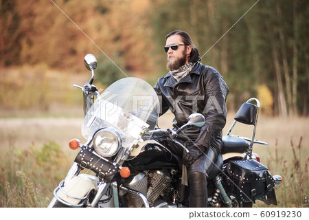 Bearded biker in black leather jacket on modern motorcycle on country roadside. Bearded biker in black leather jacket on modern motorcycle on country roadside. 60919230