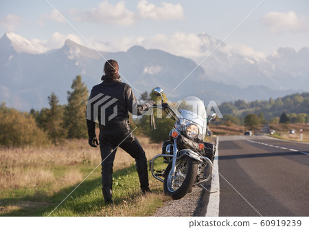 Tall athletic biker in black leather clothing standing at modern powerful high-speed motorcycle. Tall athletic biker in black leather clothing standing at modern powerful high-speed motorcycle. 60919239