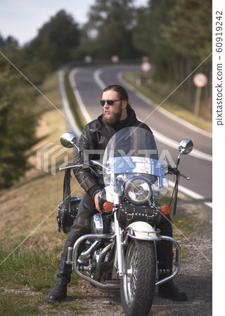 Bearded biker with long hair in black leather jacket sitting on modern motorcycle. Bearded biker with long hair in black leather jacket sitting on modern motorcycle. 60919242