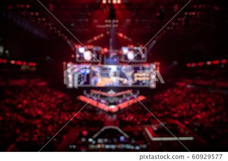 Blurred background of an esports event - Big illuminated main stage of a computer games tournament located on a big stadium. Tribunes are full of video games fans. 60929577