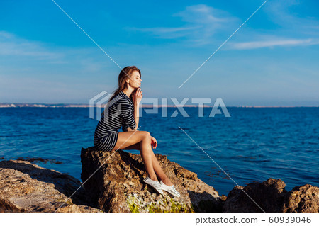 the girl in the striped dress sits on the rocks by the sea the girl in the striped dress sits on the rocks by the sea 60939046