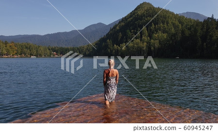 Woman walk on water on pier in sunglasses and a boho silk shawl. Girl rest on flood wood underwater dock. The pavement is covered with water in lake. Woman walk on water on pier in sunglasses and a boho silk shawl. Girl rest on flood wood underwater dock. The pavement is covered with water in lake. 60945247