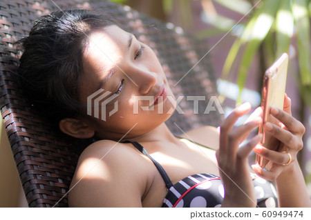 Woman sunbathing on lounger and using mobile phone Woman sunbathing on lounger and using mobile phone 60949474