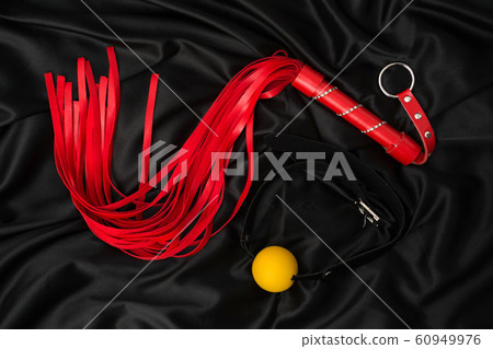 Red whip and gag on a black silk background. 60949976