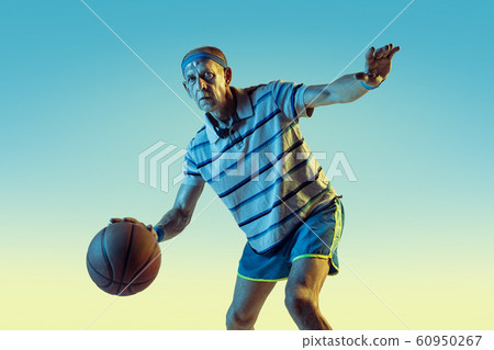 Senior man playing basketball in sportwear on gradient background and neon light 60950267