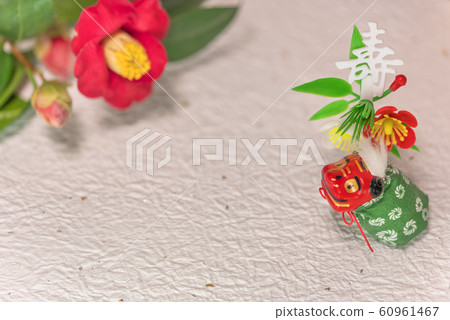 可愛的舞獅形象站在金箔紙和山茶花上,也被稱為冬玫瑰和用壽漢字裝飾 可愛的舞獅形象站在金箔紙和山茶花上,也被稱為冬玫瑰和用壽漢字裝飾 60961467