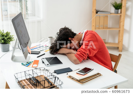 Exhausted young male freelancer napping on desk in front of computer screen 60961673