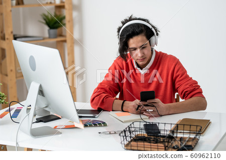 Serious guy scrolling in smartphone while listening to music during work 60962110