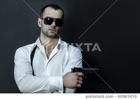 Young man in glasses wears holds a gun in his hand 60965450