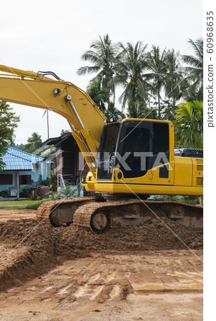Yellow excavator on a construction site against blue sky. Heavy industry. Close up details of industrial excavator. Large tracked excavator standing on a orange ground with a palms on background. Yellow excavator on a construction site against blue sky. Heavy industry. Close up details of industrial excavator. Large tracked excavator standing on a orange ground with a palms on background. 60968635