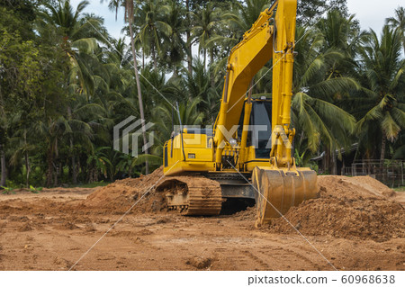 Yellow excavator on a construction site against blue sky. Heavy industry. Close up details of industrial excavator. Large tracked excavator standing on a orange ground with a palms on background. 60968638