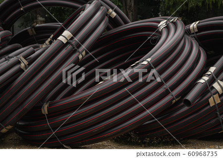 Black rubber or plastic pipes with a red lines as a construction material and equipment at building site. Using as a water pipe. 60968735