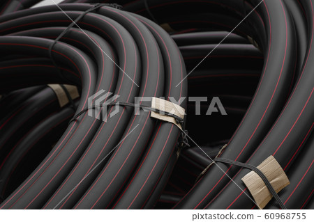Black rubber or plastic pipes with a red lines as a construction material and equipment at building site. Using as a water pipe. 60968755