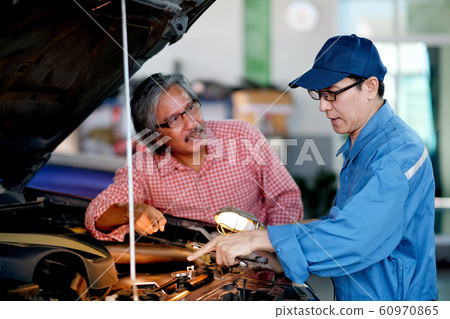 Asian automotive mechanic with blue uniform point to the car engine Asian automotive mechanic with blue uniform point to the car engine 60970865