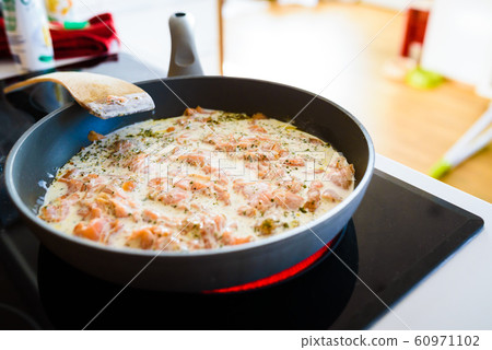 Pan with Cut Salmon Pieces in sour cream with spices on stove. in bright kitchen Pan with Cut Salmon Pieces in sour cream with spices on stove. in bright kitchen 60971102