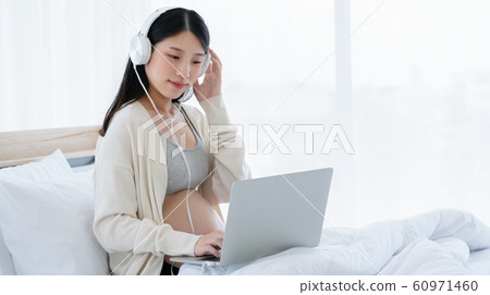 Beautiful Asian pregnant women wear headphones, use a laptop, find information about the health care 60971460