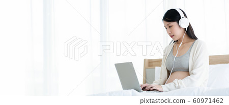 Beautiful Asian pregnant women wear headphones, use a laptop, find information about the health care 60971462