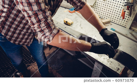 Ski maintenence. Removing excess wax from race ski base plastic scraper. Ski service and repair. Winter shop worker doing base repair. Rental workshop service. Repairman In Workshop Ski Service 60973870
