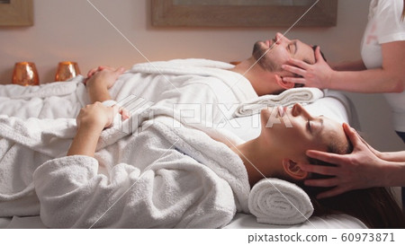 Beautiful couple lying down on massage beds enjoying a head massage in luxury spa. 60973871
