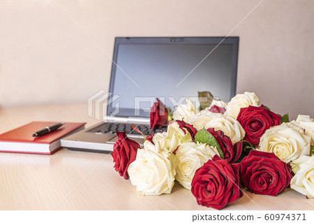 Flowers gift from fresh white and red roses at workplace on slightly pink background. On wooden table near laptop keyboard is large number of roses. Valentine concept. 60974371