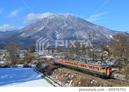 湘南色的信濃鐵路115系列列車在新鮮的雪黑姬山上行駛 60976742