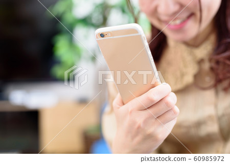 一個女人在客廳裡看著她的智能手機 一個女人在客廳裡看著她的智能手機 60985972