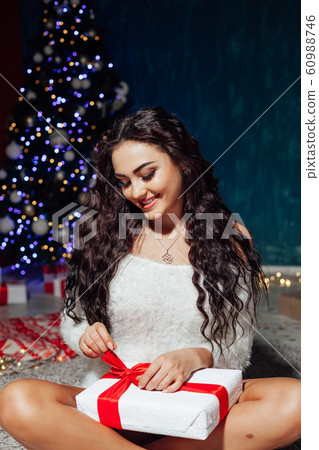 Beautiful brunette woman with gifts at the Christmas tree lights garlands new year 60988746