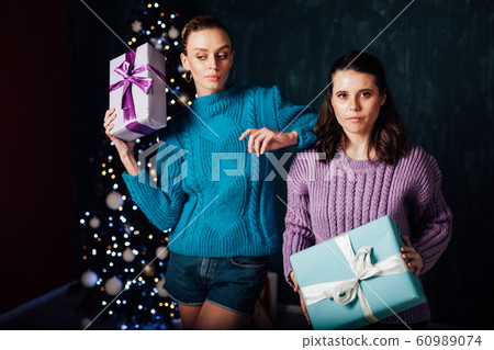 Two beautiful female girlfriends open Christmas gifts at the Christmas tree for the New Year holiday 60989074