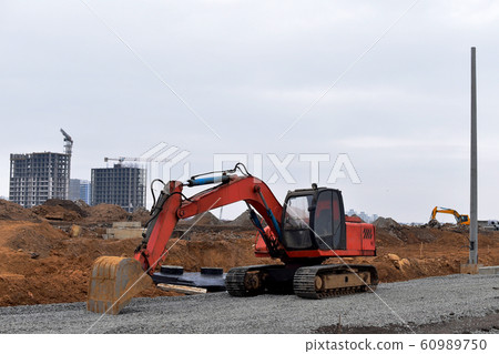 Excavator with a large iron bucket on a construction site during road works. Excavator with a large iron bucket on a construction site during road works. 60989750