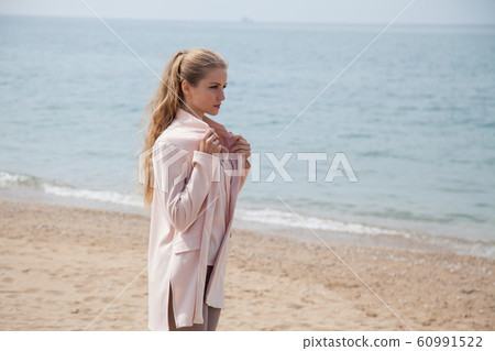 Beautiful blonde woman in walks alone on an empty beach by the sea Beautiful blonde woman in walks alone on an empty beach by the sea 60991522