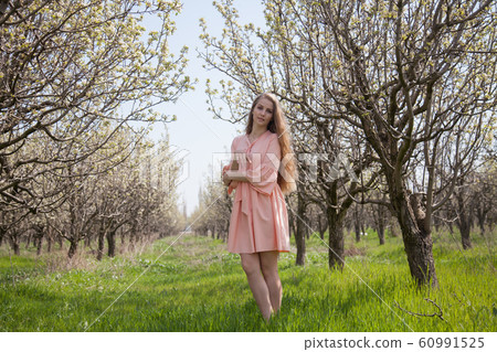 Beautiful blonde woman in pink dress in green flowering garden in spring Beautiful blonde woman in pink dress in green flowering garden in spring 60991525