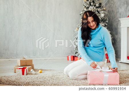 a pregnant woman sitting by the Christmas tree opens Christmas presents a pregnant woman sitting by the Christmas tree opens Christmas presents 60991934