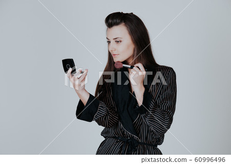 girl in coat makes brush makeup looks in the mirror 60996496