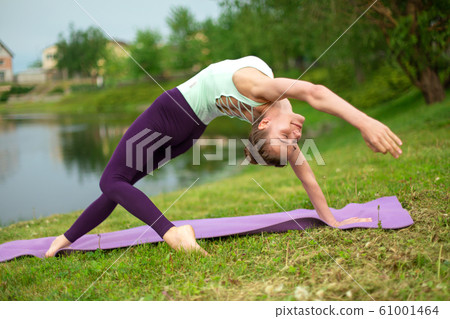 A young sports girl practices yoga on a green lawn A young sports girl practices yoga on a green lawn 61001464