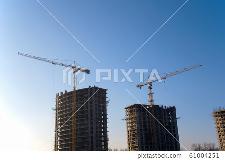 Tower cranes constructing a new residential building at a construction site against blue sky.  61004251