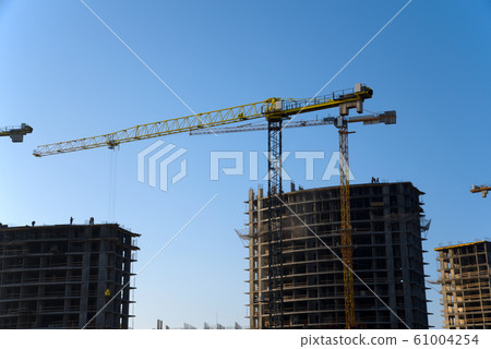 Tower cranes constructing a new residential building at a construction site against blue sky.  61004254