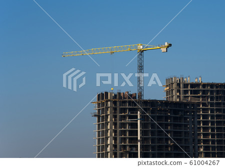 Tower crane constructing a new residential building at a construction site against blue sky. 61004267