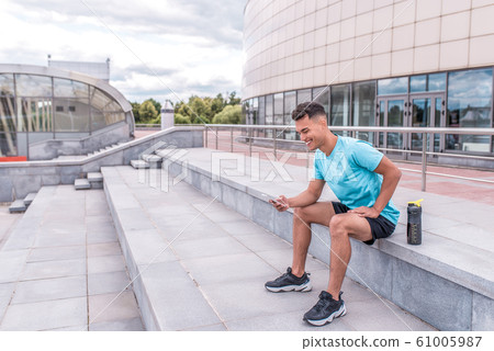 Young sportsman, male athlete, happy smiling, laughing hands of phone, rest after workout, fitness, active lifestyle modern youth, sportswear. Motivation for life. Free space and copy text. Young sportsman, male athlete, happy smiling, laughing hands of phone, rest after workout, fitness, active lifestyle modern youth, sportswear. Motivation for life. Free space and copy text. 61005987