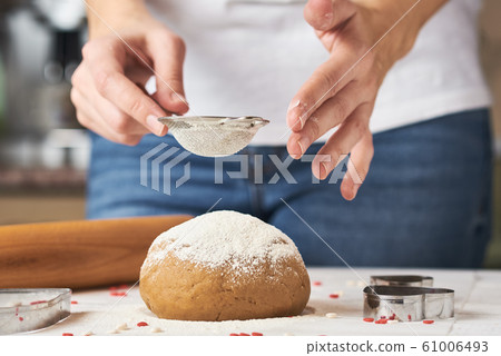 Woman sprinkling flour over fresh dough  61006493