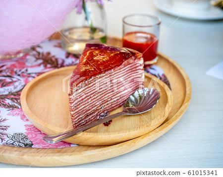 A piece of strawberry jam crepe cake on wooden round plate 61015341