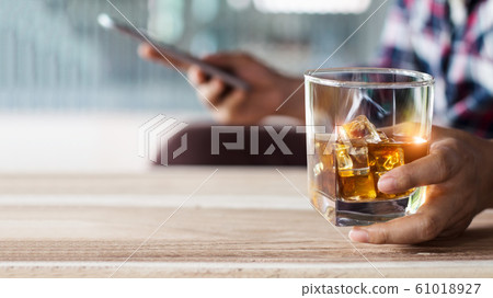 Man relaxing whith bourbon whiskey drink alcoholic beverage and using mobile smartphone. Man relaxing whith bourbon whiskey drink alcoholic beverage and using mobile smartphone. 61018927