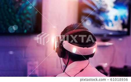 Young gamer wearing VR goggles and headset playing and winning driver and shooter online video game on his personal computer in the room lit by neon lights. VR, eSport network online.g Young gamer wearing VR goggles and headset playing and winning driver and shooter online video game on his personal computer in the room lit by neon lights. VR, eSport network online.g 61018936