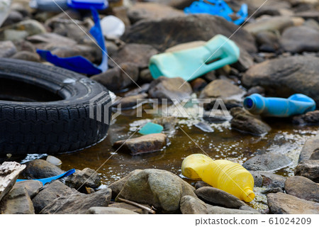 Plastic bottles and car tire in muddy oily water stream 61024209