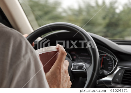 The car driver holds a coffee cup in hand 61024571