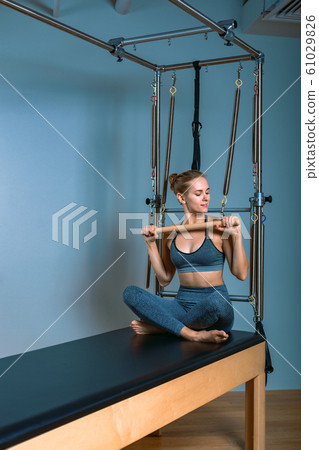 Young girl doing pilates exercises with a reformer bed. Beautiful slim fitness trainer on reformer gray background, low key, art light. Fitness concept Young girl doing pilates exercises with a reformer bed. Beautiful slim fitness trainer on reformer gray background, low key, art light. Fitness concept 61029826