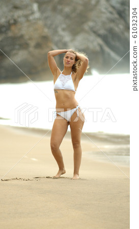 Beautiful woman poses for the camera on a beach at the ocean Beautiful woman poses for the camera on a beach at the ocean 61032304